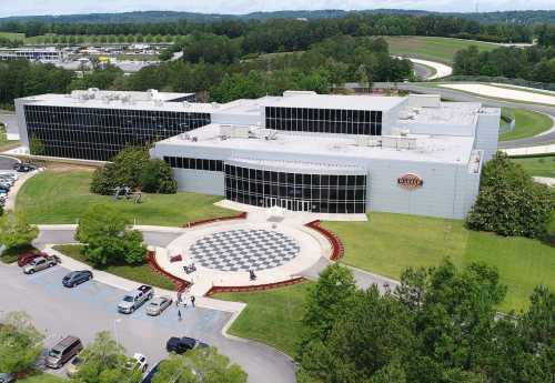 Aerial view of a modern building with a checkered pattern entrance, surrounded by greenery and parked cars.