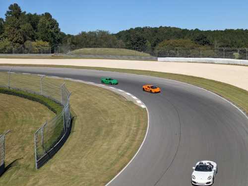 Two sports cars, one green and one orange, race around a curve on a racetrack with trees in the background.