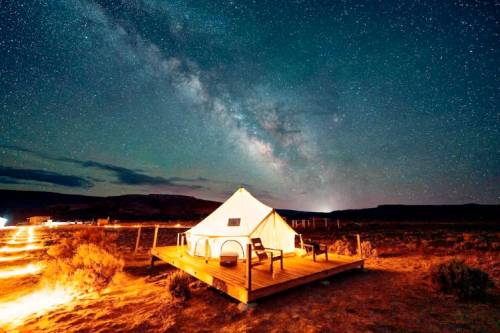A glamping tent on a wooden deck under a starry sky with the Milky Way visible in the background.