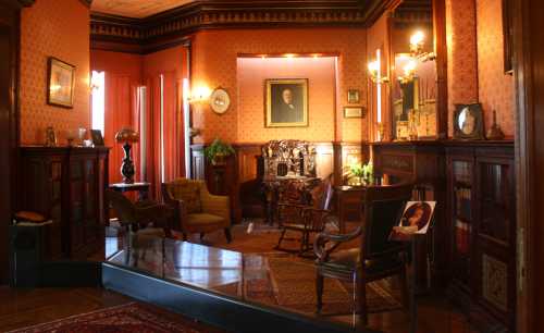 A vintage room with ornate woodwork, a portrait on the wall, and elegant furniture, creating a cozy, historical atmosphere.