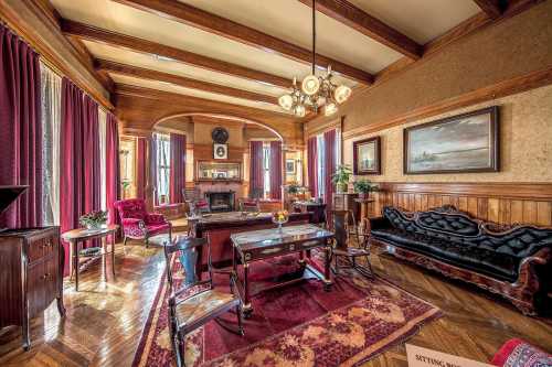 Elegant living room with wooden beams, rich red curtains, vintage furniture, and a cozy fireplace.