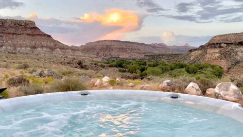 A hot tub overlooking a scenic desert landscape with mountains and a colorful sunset in the background.