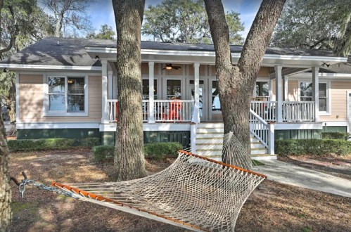 A cozy house with a porch, surrounded by trees, featuring a hammock strung between two large trunks.