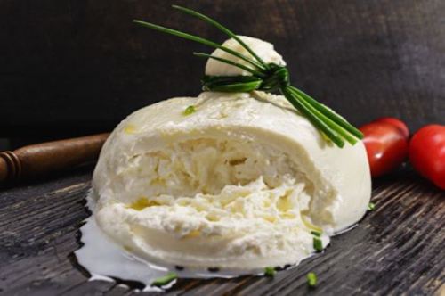 A creamy cheese ball topped with chives, resting on a wooden surface, with cherry tomatoes nearby.