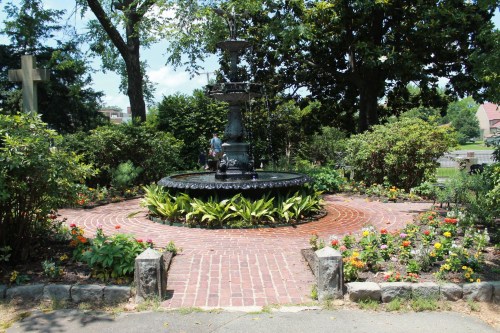 A decorative fountain surrounded by colorful flowers and greenery in a peaceful garden setting.
