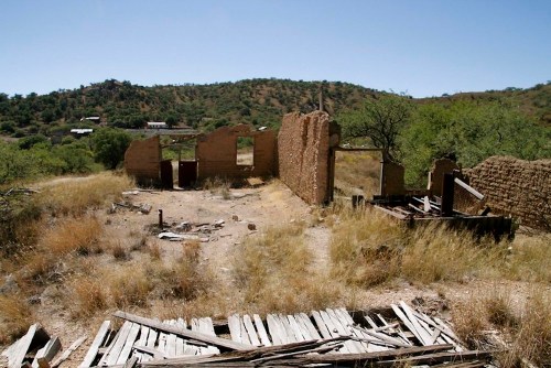 Abandoned ruins of a building surrounded by dry grass and sparse trees under a clear blue sky.