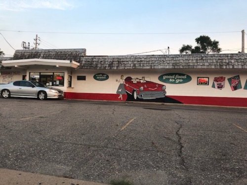 A retro-style diner with a mural of a red convertible and the text "good food to go" on the wall.