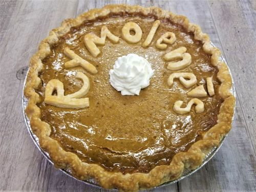 A pumpkin pie with a decorative crust spelling "Pymolenes" and topped with a dollop of whipped cream.