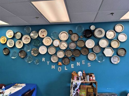A blue wall adorned with various decorative plates arranged in a creative pattern, with the word "RYMLENES" below.