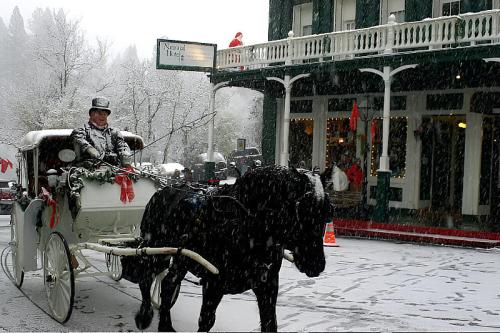 A horse-drawn carriage in a snowy scene, with a driver in formal attire and festive decorations on a building nearby.