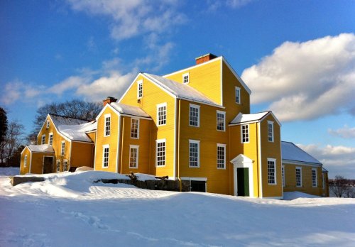 A large yellow house with multiple gables, surrounded by snow under a blue sky with fluffy clouds.