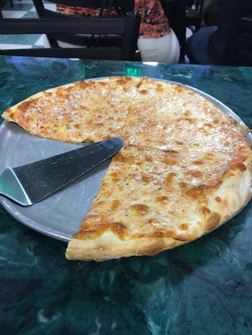 A silver pizza tray with a slice of cheese pizza, partially cut, on a green marble table.