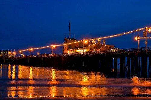 A pier at dusk, illuminated by warm lights reflecting on the water, creating a serene coastal atmosphere.