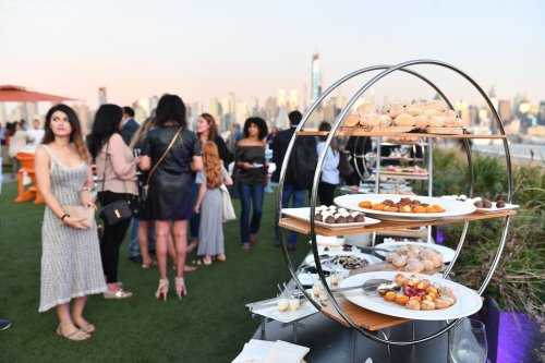 A tiered dessert display with various pastries, set against a skyline backdrop and guests mingling in the background.