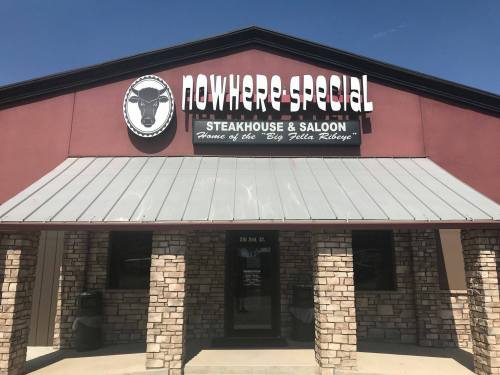 Sign for "Nowhere Special Steakhouse & Saloon" with a cow logo, featuring a stone facade and a metal roof.