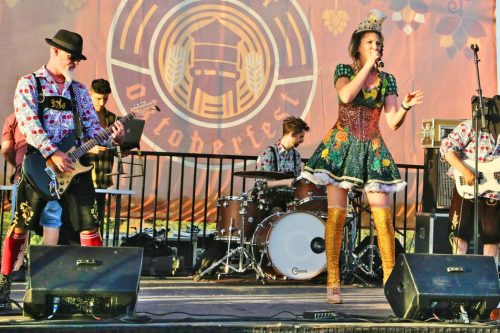 A lively band performs on stage, featuring a singer in a colorful dress and musicians playing guitar and drums.