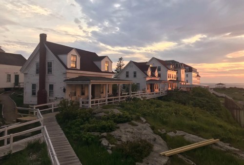 A scenic view of coastal houses at sunset, with a wooden walkway and lush greenery in the foreground.