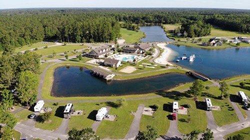 Aerial view of a resort with a pool, surrounded by water and greenery, with RVs parked nearby.