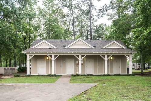 A small, light-colored building with multiple doors, surrounded by trees and grass in a park-like setting.