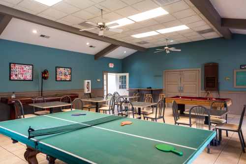 A spacious game room with a ping pong table, chairs, and a pool table, featuring teal walls and bright lighting.