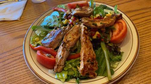 A colorful salad topped with grilled chicken, tomatoes, corn, and mixed greens on a plate.