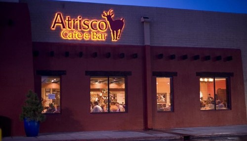 Exterior of Atrisco Cafe & Bar at dusk, featuring a lit sign and large windows showing diners inside.