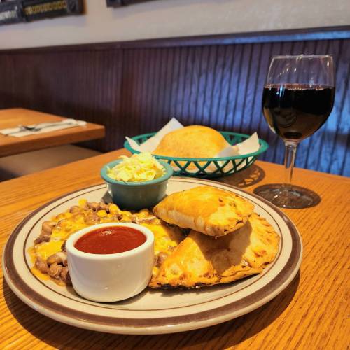 A plate of cheesy beef enchiladas with salsa, a side of coleslaw, a bread roll, and a glass of red wine.