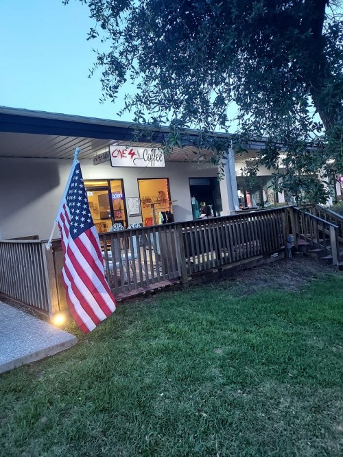 A coffee shop with a wooden deck, featuring an American flag in front and people visible inside.