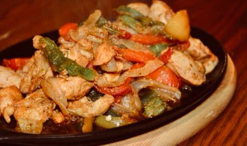 Sizzling platter of chicken fajitas with bell peppers and onions, served on a wooden board.