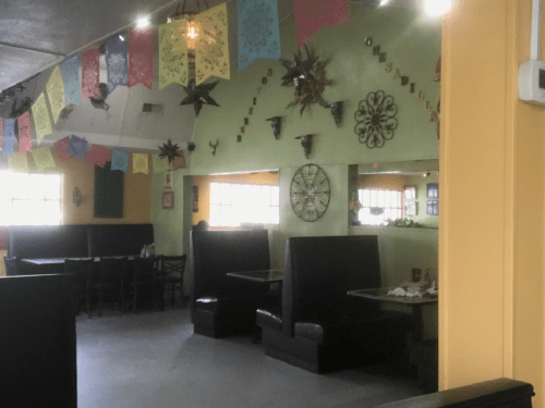 Colorful papel picado decorations hang in a vibrant restaurant with black booths and a bright green wall.
