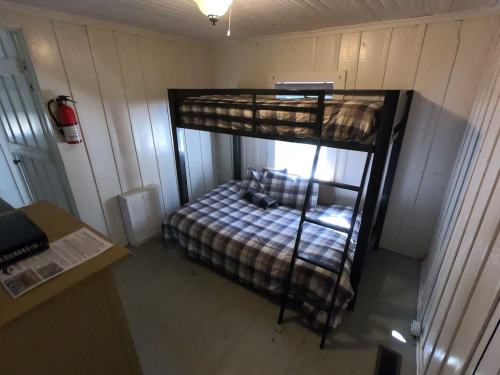A small room with a bunk bed and a double bed, featuring plaid bedding and a window with natural light.