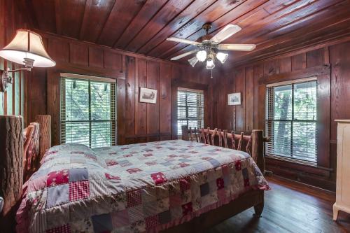 Cozy bedroom with wooden walls, a quilted bedspread, ceiling fan, and windows letting in natural light.