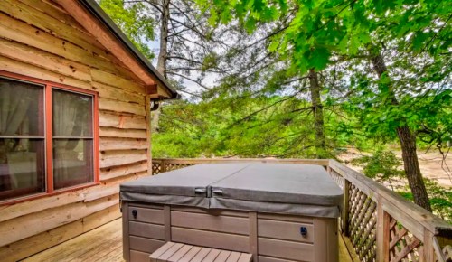 A wooden cabin deck featuring a hot tub surrounded by lush green trees.