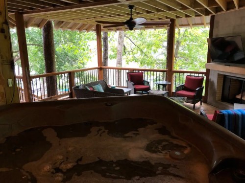 A cozy porch with a hot tub, seating area, and trees visible through the railing.