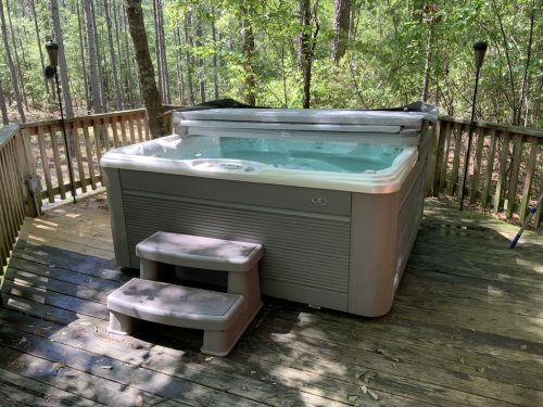 A hot tub on a wooden deck surrounded by trees, with steps leading up to it.