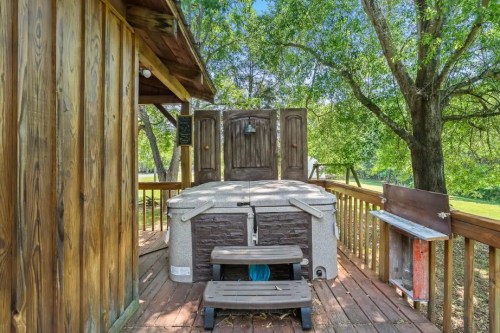 A wooden deck with a hot tub surrounded by trees and a rustic wooden structure in the background.