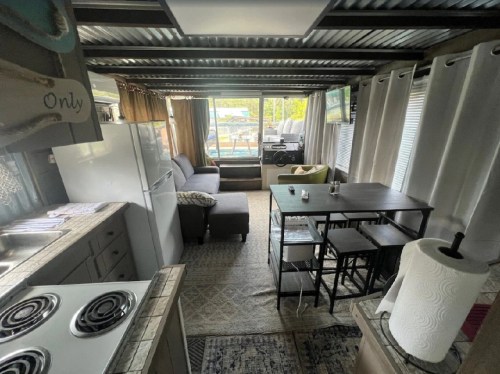 Cozy interior of a small cabin with a kitchen, dining area, and living space, featuring large windows and modern decor.
