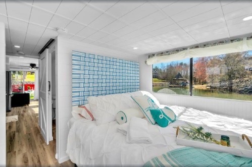 Cozy bedroom with a large window overlooking a lake, featuring a patterned wall and white bedding.