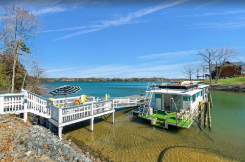 A serene lakeside view featuring a dock, a houseboat, and clear blue skies.