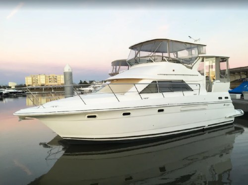 A white yacht docked at a marina during sunset, with calm waters and buildings in the background.