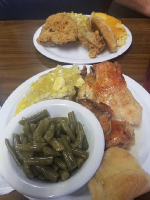 A plate of fried chicken, green beans, rice with gravy, and a biscuit, with another plate of food in the background.