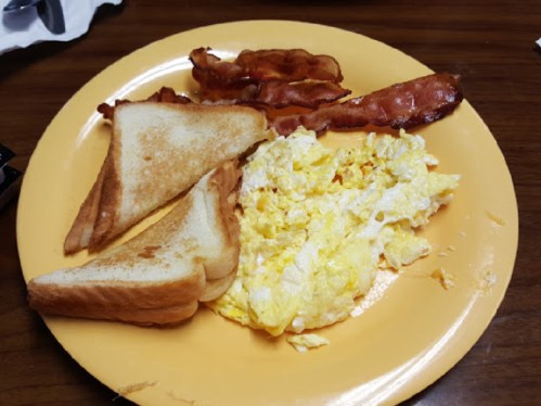 A plate with scrambled eggs, crispy bacon, and two slices of toasted bread.