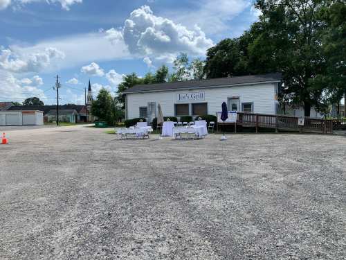 Outdoor view of Joe's Grill with tables set up for an event, surrounded by a gravel parking lot and trees.