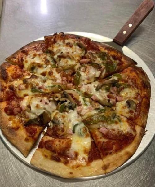 A freshly baked pizza topped with cheese, green peppers, and ham, sliced into eight pieces on a metal tray.