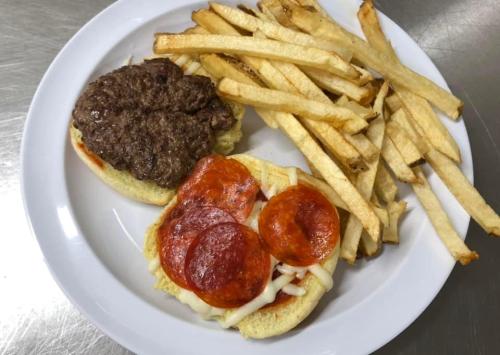 A plate with a burger topped with ground beef and pepperoni, served with a side of crispy French fries.