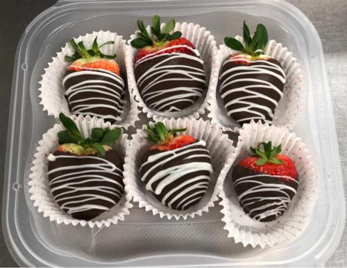 A clear container holding six chocolate-covered strawberries drizzled with white chocolate.