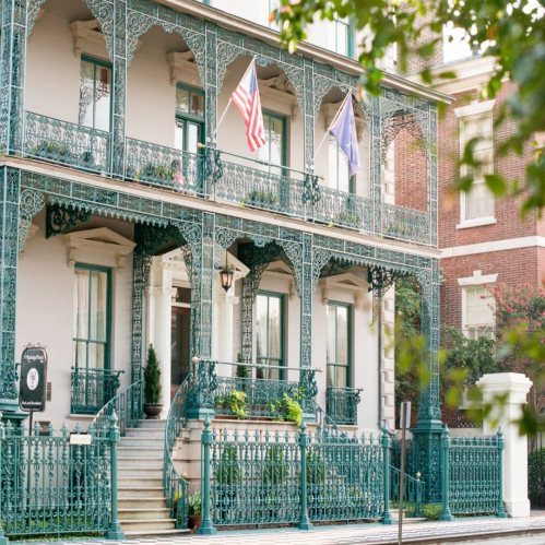 Historic building with intricate ironwork balconies, featuring American flags and lush greenery.