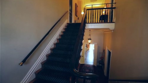 A staircase with dark green carpet leads to an upper floor, illuminated by warm lighting and framed by a hallway.