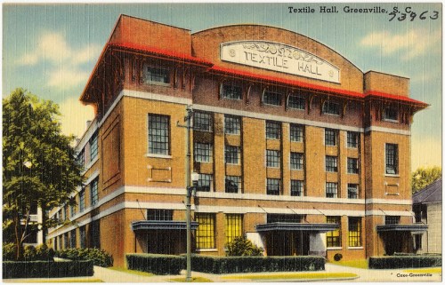 Historic Textile Hall building in Greenville, SC, featuring a red roof and large windows, surrounded by greenery.