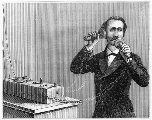 A historical illustration of a man using an early telephone, speaking into a receiver connected to a device.